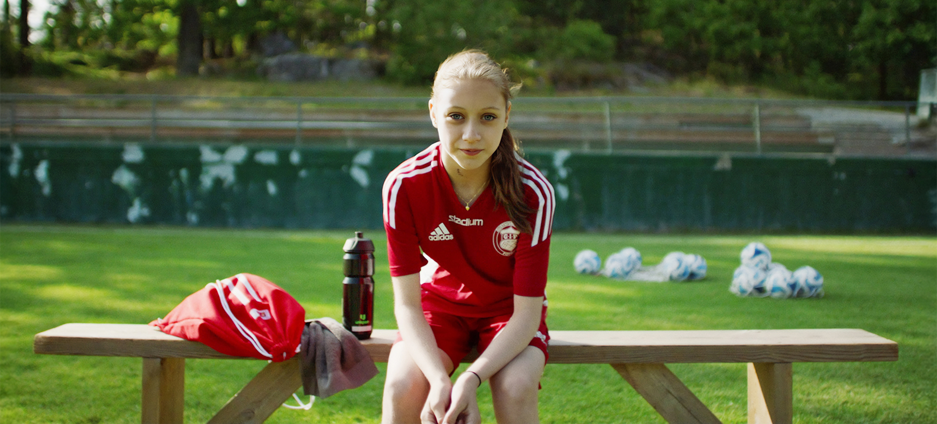 Girl in football outfit sitting on a bench on football field