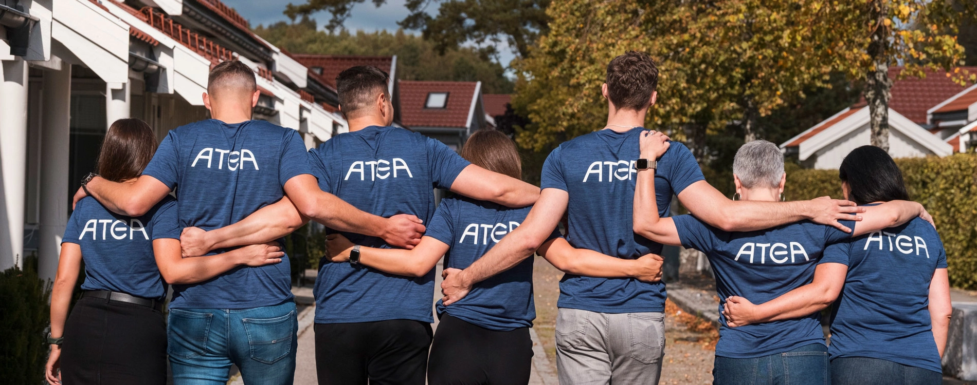 Seven People Walking With Their Backs Turned And Atea Logo On Their T Shirts